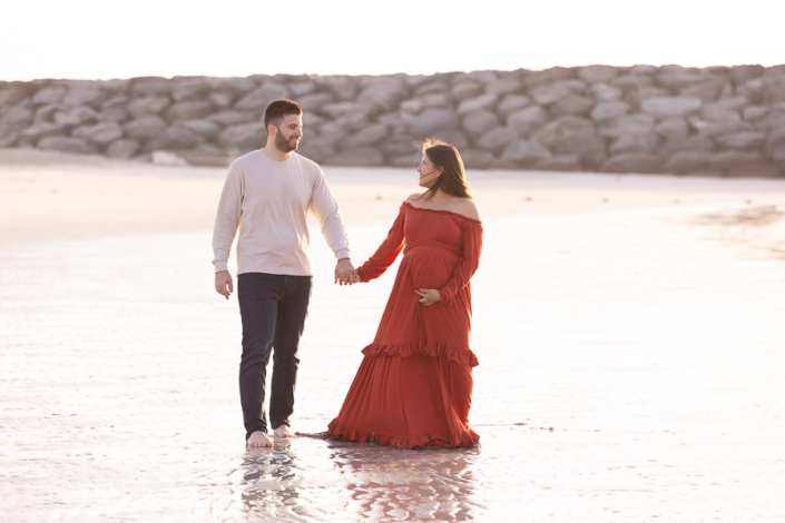regnant mother walking along the sand at Al Mamzar Beach between Dubai and Sharjah during a maternity photoshoot, with calm water beside her