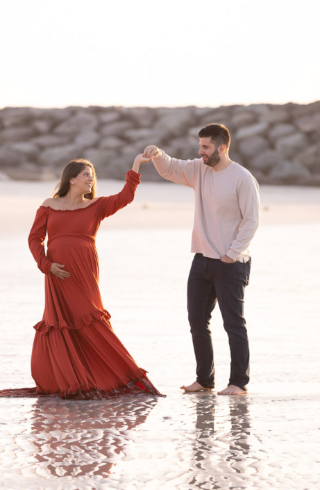 “Pregnant woman walking along Al Khan Beach in Sharjah during golden hour, with soft golden sand and calm turquoise water behind her