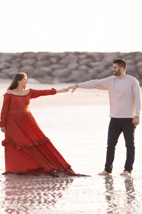 Close‑up of an expecting mother’s hands resting on her baby bump during a maternity photoshoot at Jumeirah Beach in Dubai, with the sea softly blurred behind