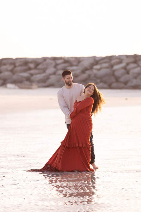 Pregnant woman lying on her side on the sand at a Palm Jumeirah beach in Dubai during a maternity photoshoot, resting her head on her hand.