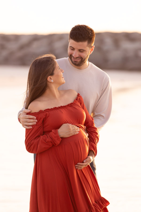 Pregnant woman laughing during a maternity photoshoot at Kite Beach in Dubai, with her partner just out of frame making her smile