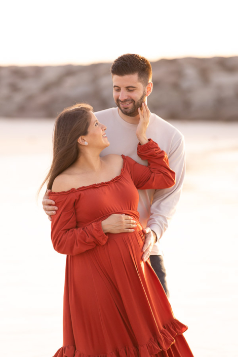 Back view of a pregnant woman in a long dress walking towards the water at Al Sufouh Beach in Dubai during a maternity photoshoot.