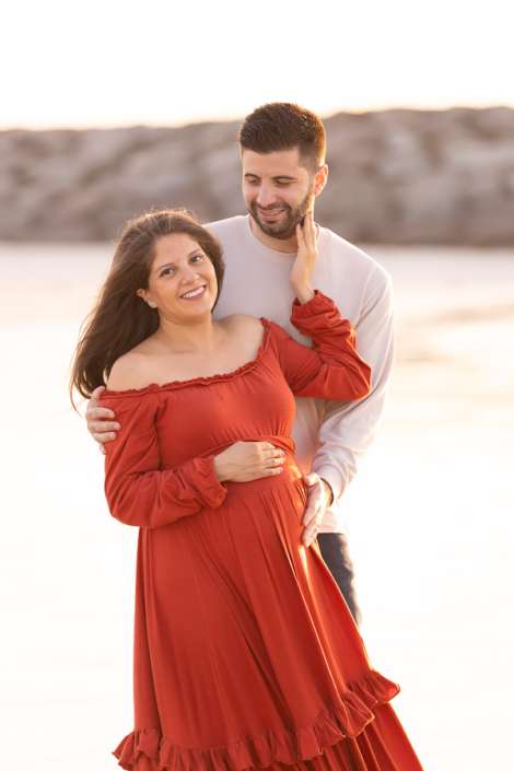 Expecting couple in a close embrace on Jumeirah Beach in Dubai during a maternity photoshoot, with the ocean softly blurred behind them.