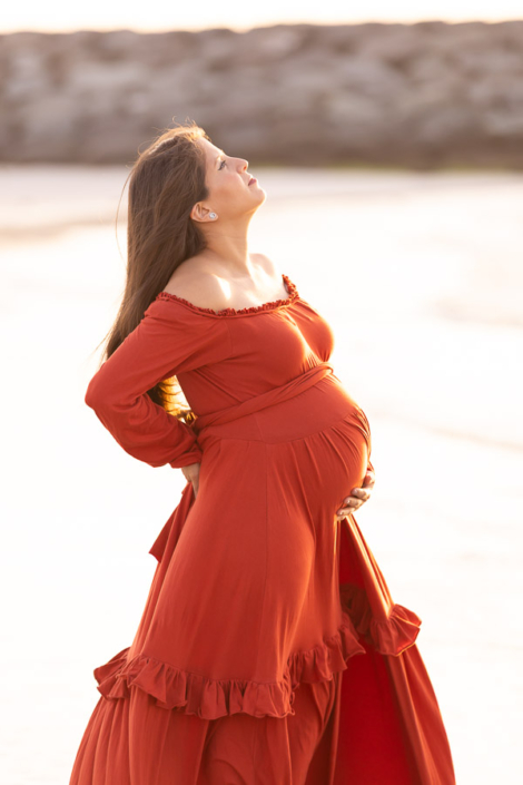 Expecting couple sitting on a blanket at Kite Beach in Dubai during a maternity photoshoot, with their hands resting on the baby bump.