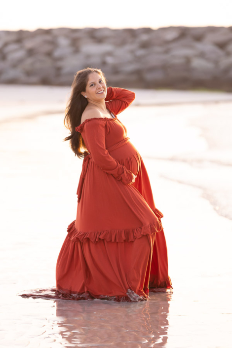 Pregnant woman at Al Sufouh Beach in Dubai, looking off to the side towards her partner with a soft smile during a maternity photoshoot