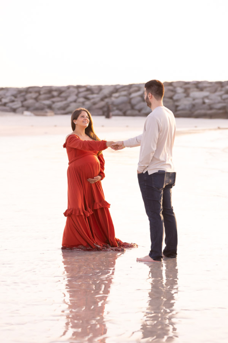 Pregnant woman twirling in a long flowing gown on Jumeirah Beach in Dubai during a maternity photoshoot, with the fabric lifting in the sea breeze.