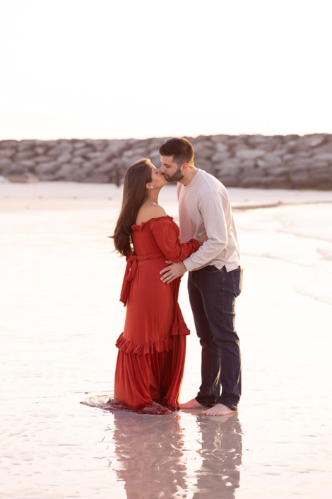 Silhouette of a pregnant woman standing on Al Sufouh Beach in Dubai at sunset, with the sun setting behind her and the waves at her feet.