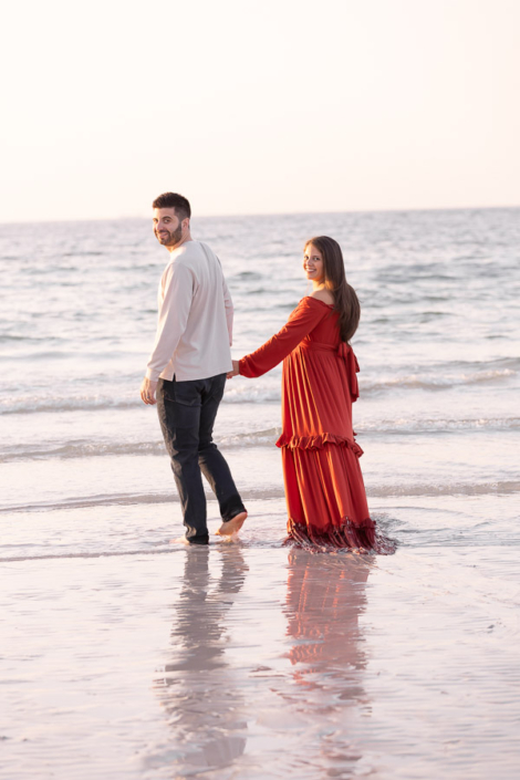 Expecting father standing behind his pregnant partner at Kite Beach in Dubai, hands on her baby bump as they look towards the ocean.