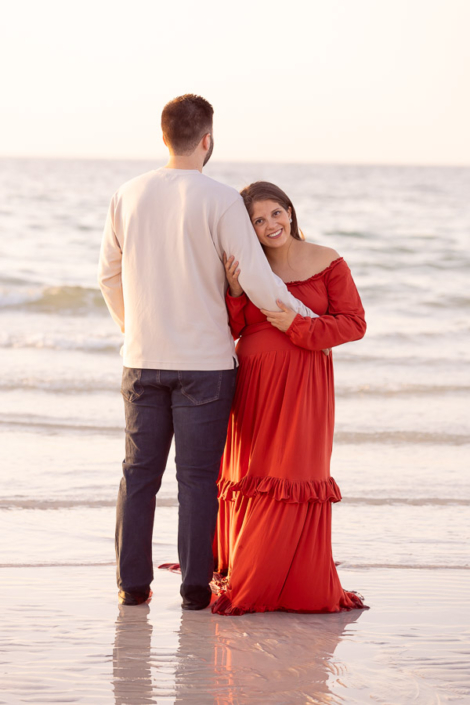 Pregnant woman walking barefoot along Kite Beach in Dubai during a maternity photoshoot, laughing as the water touches her feet