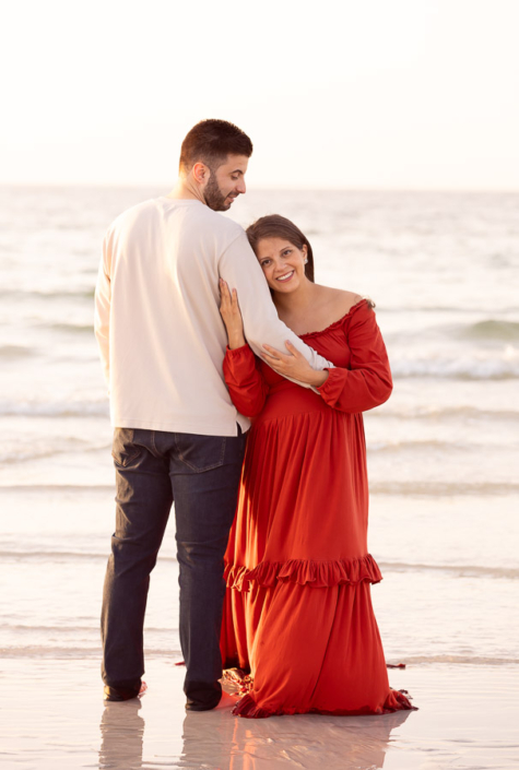 Pregnant woman sitting on the sand at Al Sufouh Beach in Dubai, gently cradling her bump and looking down with a soft smile