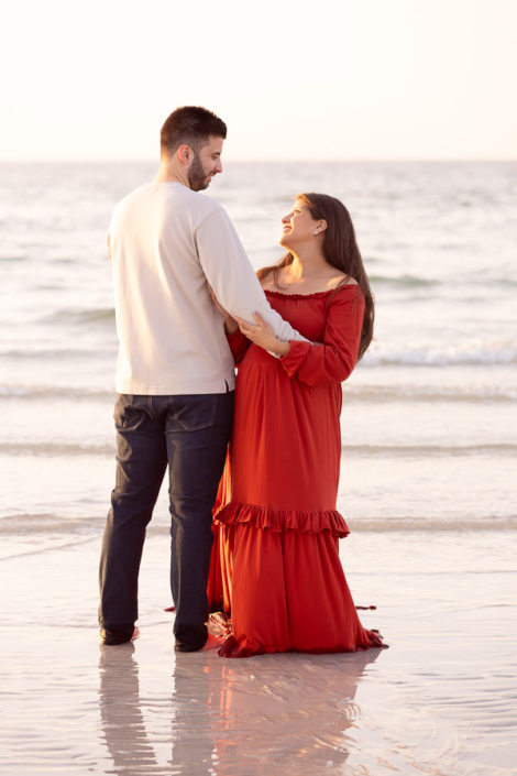 Wide angle maternity photo of a pregnant woman walking along Al Sufouh Beach in Dubai, with her dress flowing and the skyline faintly visible