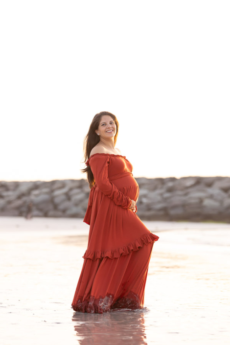 Expecting couple standing together on Jumeirah Beach in Dubai during a maternity photoshoot, smiling at each other with the sea in the background