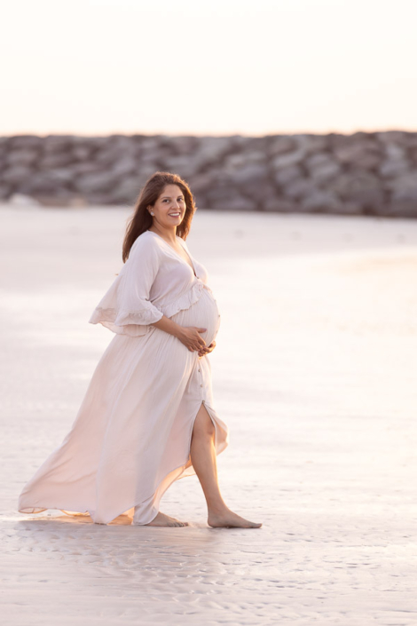 Soft close‑up of a pregnant mother holding her baby bump during a sunset maternity photoshoot at Jumeirah Beach in Dubai, with gentle waves behind her