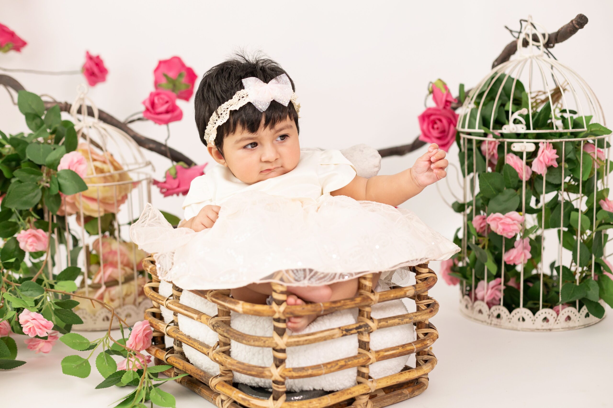 Baby girl in white dress sitting in a basket with roses during baby photography in Dubai