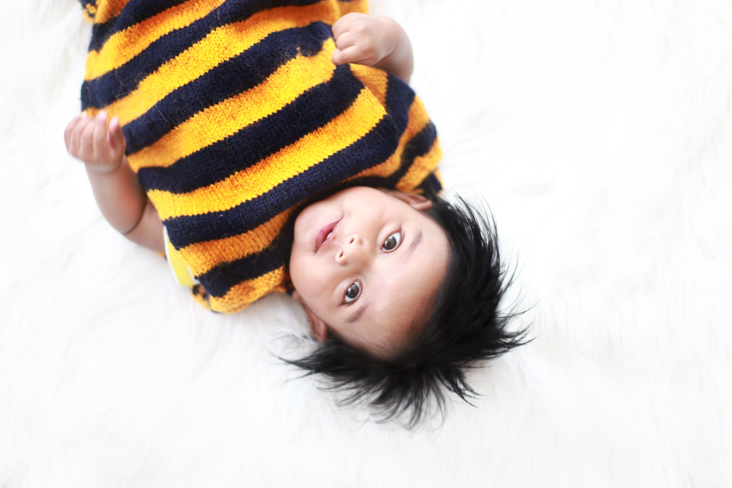Baby lying on a white backdrop wearing a striped sweater during baby photography in Dubai