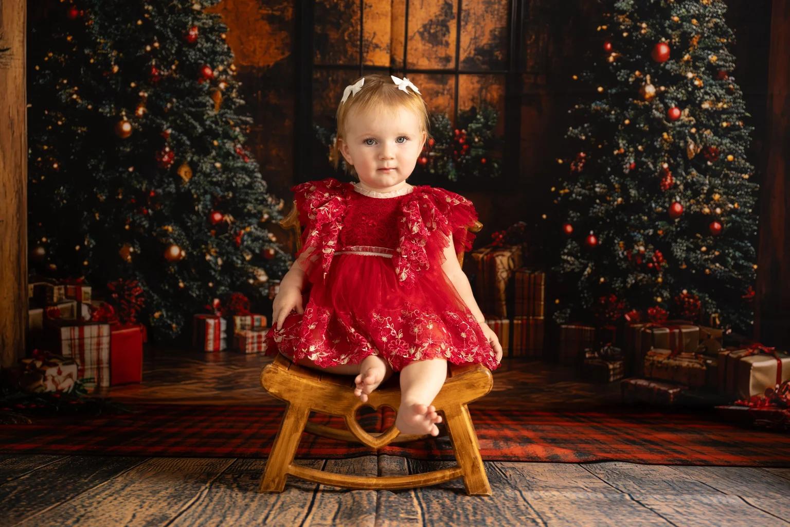Baby girl in red dress sitting in front of Christmas trees during a baby photoshoot in Dubai