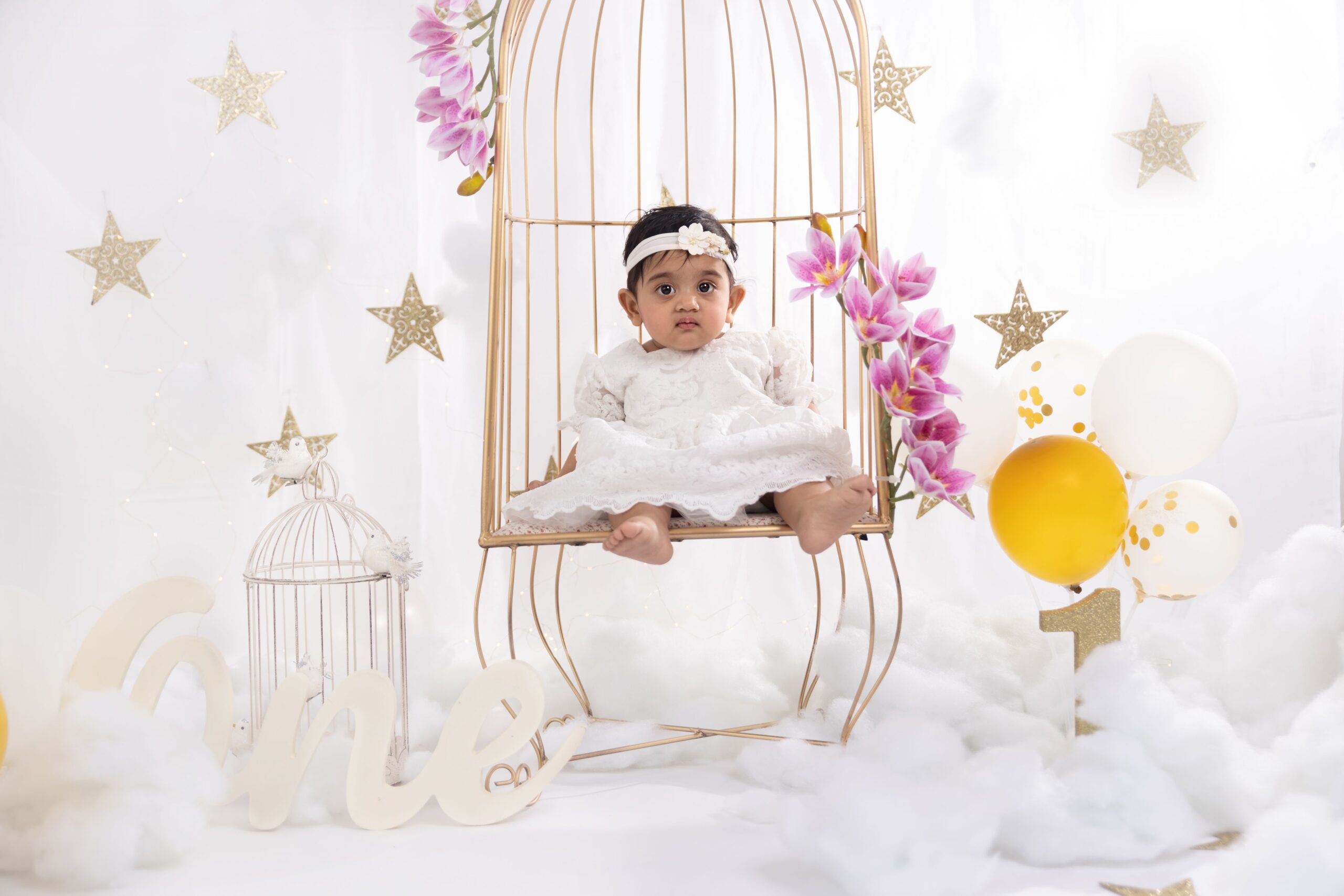 Baby girl in a white lace dress sitting on a birdcage chair in a baby photography session in Dubai